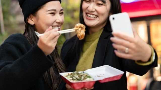 Dos chicas jóvenes japonesas en la calle comiendo y haciéndose un selfi. (Foto: Freepik)